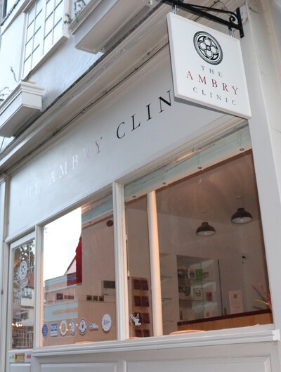 Street level view of The Ambry Clinic, with a hanging clinic sign, displaying The Ambry Clinic logo and name, above large front windows